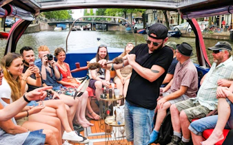 Amsterdam canal cruise with people enjoying a covered heated boat, featuring a musician playing.
