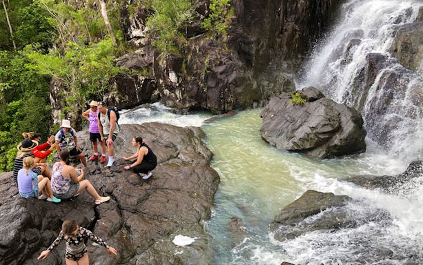 Group of tourists exploring rocky waterfall area on Falls to Paradise Guided Day Tour.