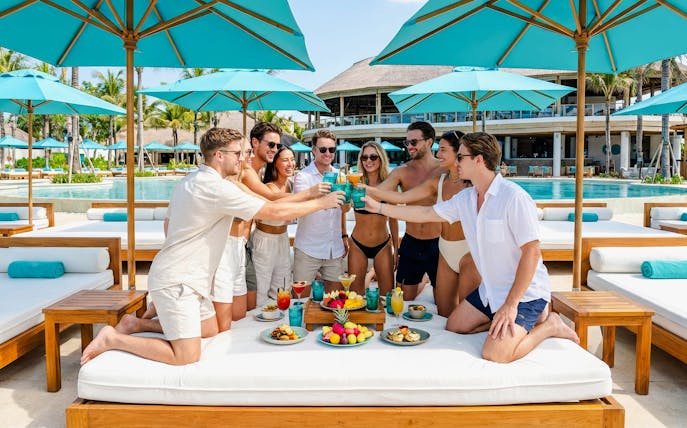 Group enjoying drinks at FINNS Beach Party Lagoon Zone on a super bed by the pool.