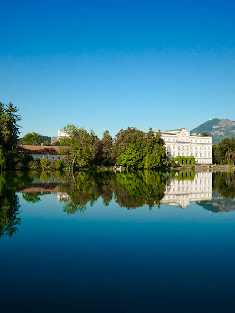 Leopoldskron Palace reflecting in a lake with mountains in Salzburg, Austria.