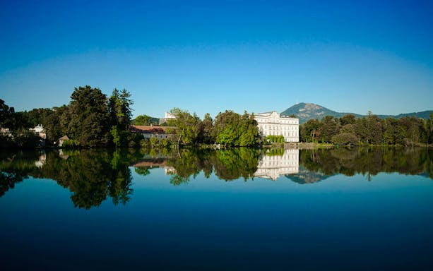 Leopoldskron Palace reflecting in a lake with mountains in Salzburg, Austria.