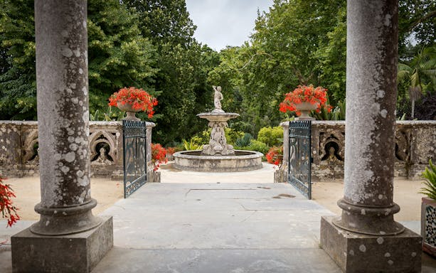 Monserrate Palace garden with stone fountain and vibrant red flowers.
