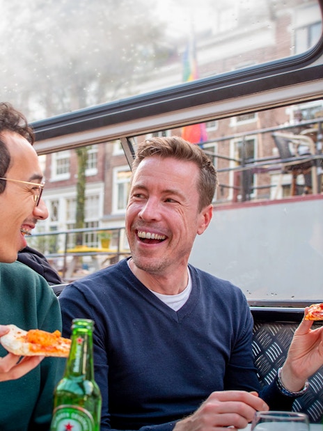 Two people enjoying pizza and drinks on an Amsterdam canal cruise.