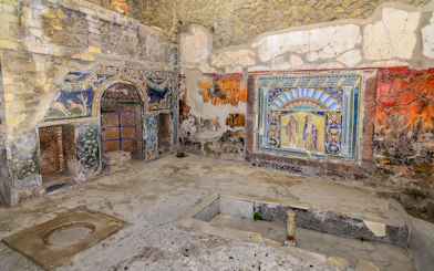 Remains of Herculaneum house interiors with frescoes and mosaics on walls.