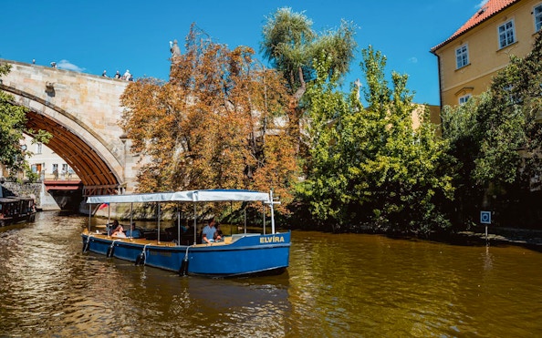 Sightseeing cruise boat on Devils Channel in Prague passing under a stone bridge.