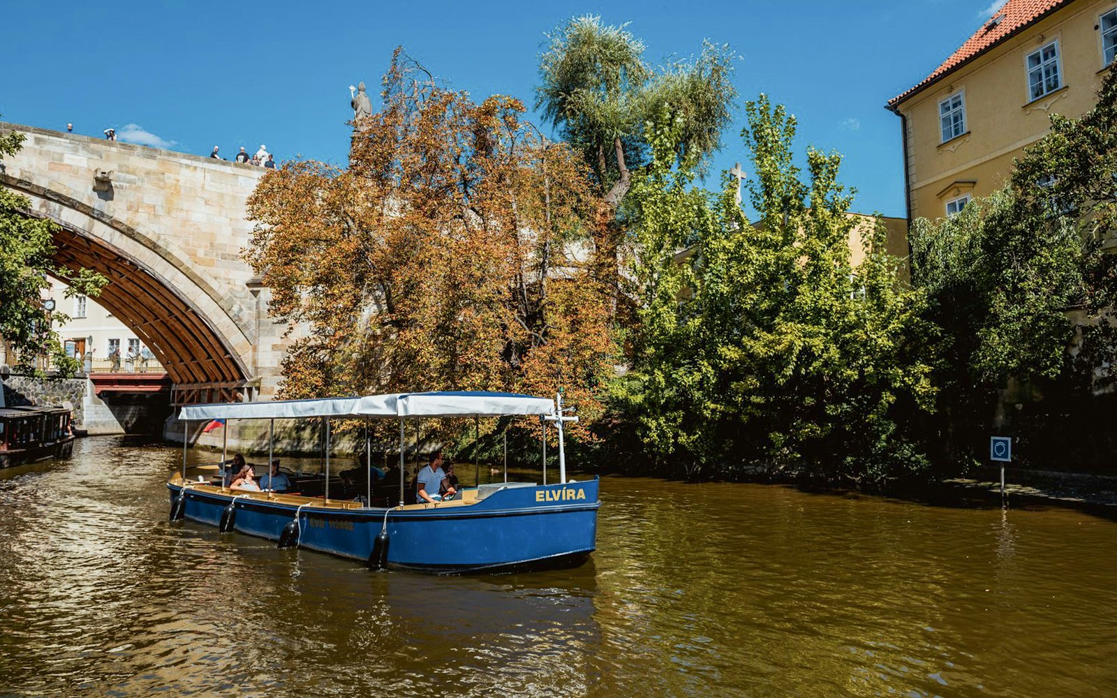 Sightseeing cruise boat navigating Devils Channel in Prague with historic buildings in the background.