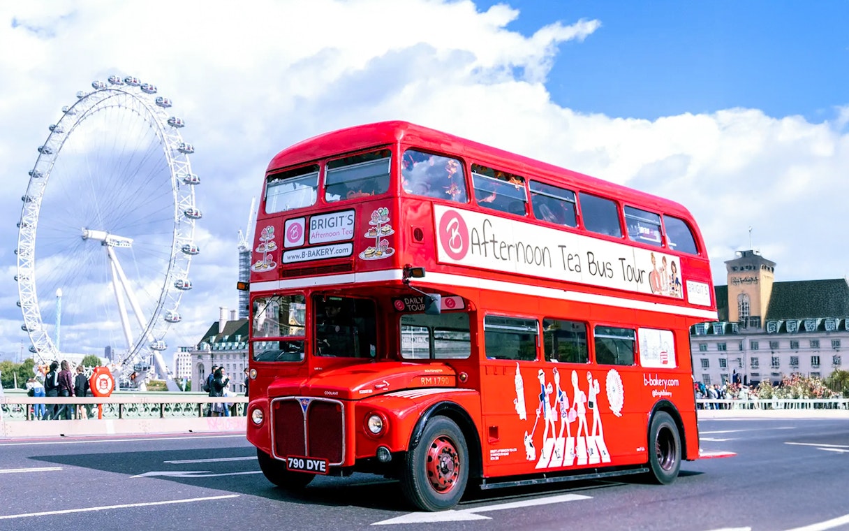 Red double-decker bus for afternoon tea tour in London with London Eye in background.