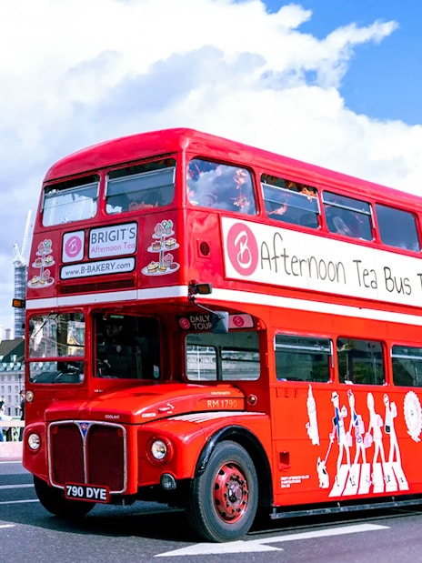 Red double-decker bus for afternoon tea tour in London with London Eye in background.