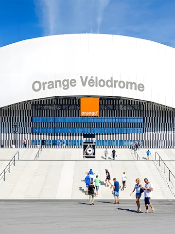 Visitors walking towards the entrance of Orange Vélodrome stadium in Marseille, France.