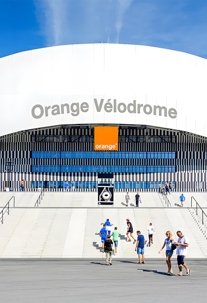 Visitors walking towards the entrance of Orange Vélodrome stadium in Marseille, France.