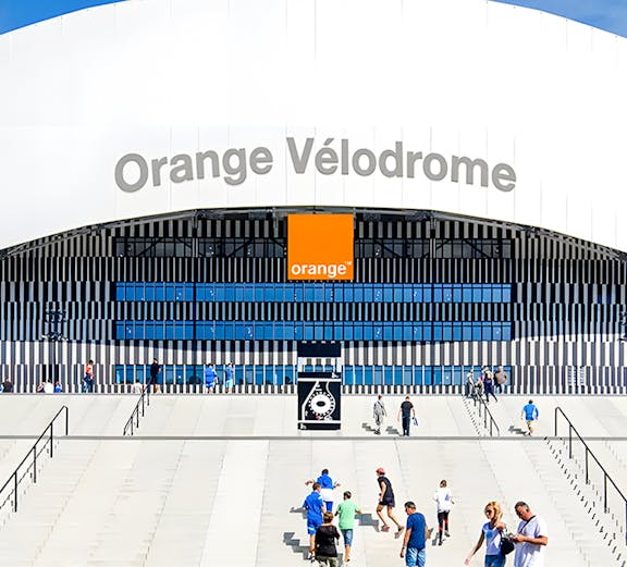 Visitors walking towards the entrance of Orange Vélodrome stadium in Marseille, France.