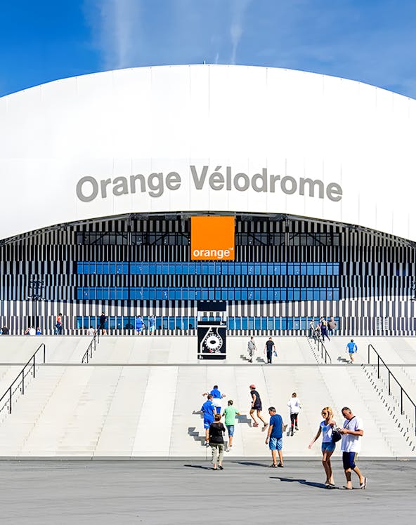 Visitors walking towards the entrance of Orange Vélodrome stadium in Marseille, France.