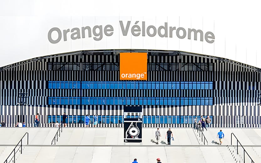 Visitors walking towards the entrance of Orange Vélodrome stadium in Marseille, France.