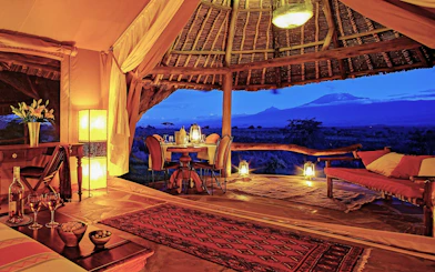 Luxury tent interior with dining setup overlooking Maasai Mara landscape at sunset.