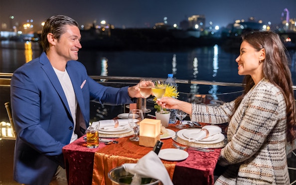 Couple toasting on Dubai Canal cruise at night with city lights in background.