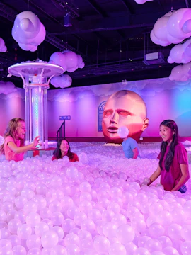 Visitors enjoying a ball pit at Bubble Planet Atlanta with colorful lighting and decor.