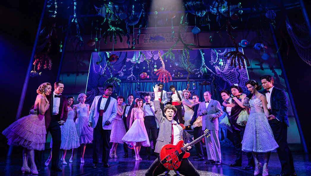 Cast performing a musical number in "Back to the Future the Musical" with vibrant stage decor.