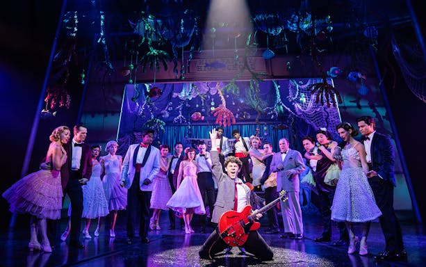 Cast performing a musical number in "Back to the Future the Musical" with vibrant stage decor.