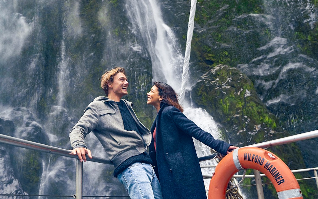 Couple enjoying Milford Sound waterfall view on cruise deck.