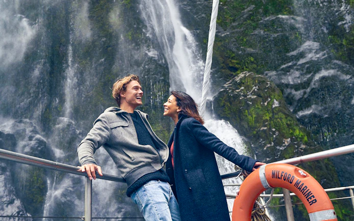 Couple enjoying Milford Sound waterfall view on cruise deck.