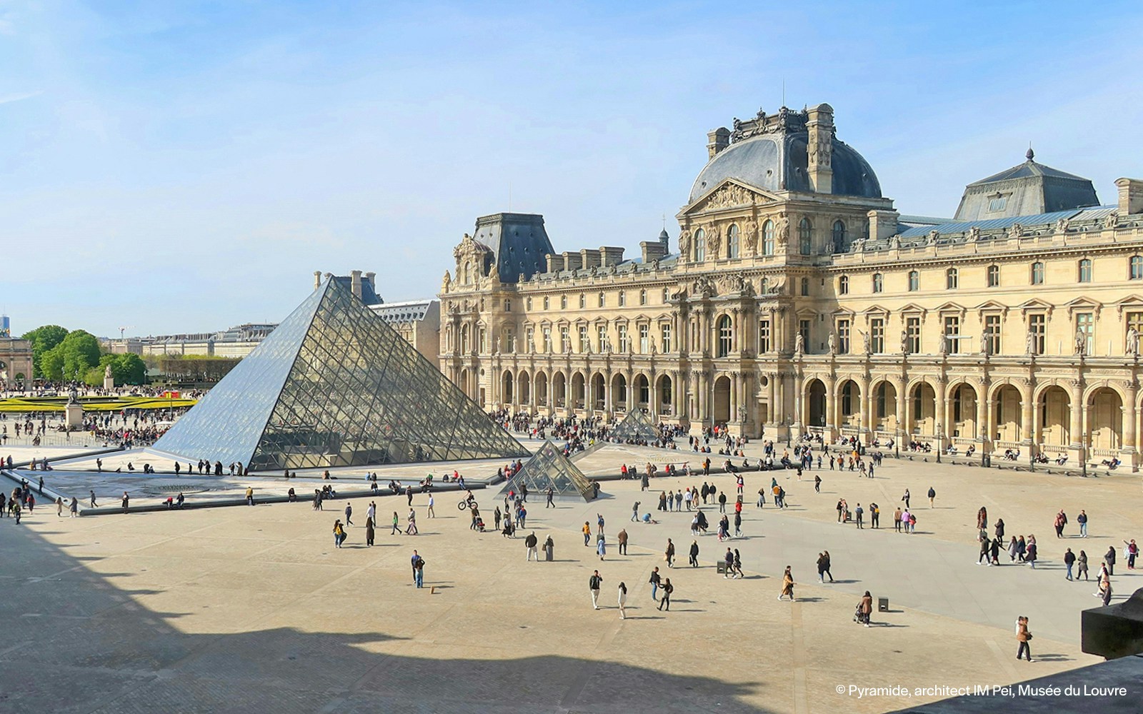 Die gläserne Pyramide und der Innenhof des Louvre in Paris, umgeben von historischen Gebäuden und Besuchern