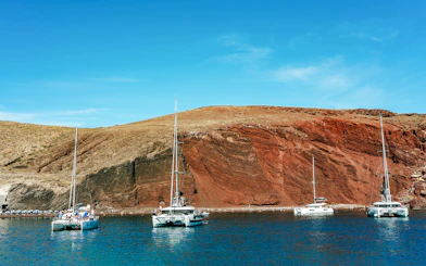 Catamarans sailing near the red beach in Santorini during the Joy Daytime Cruise.