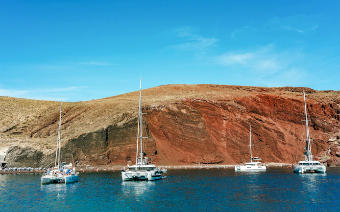 Catamarans sailing near the red beach in Santorini during the Joy Daytime Cruise.