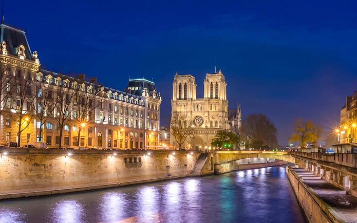 Notre Dame Cathedral illuminated at night along the Seine River in Paris.
