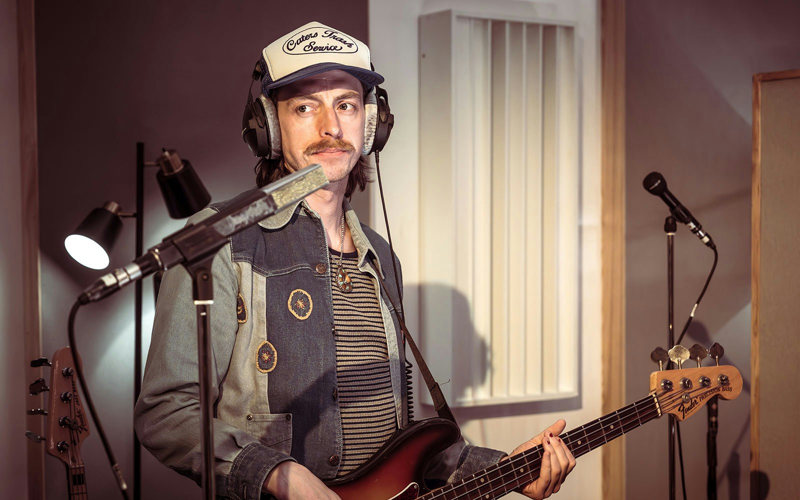 Musician playing bass guitar in a recording studio with stereophonic equipment.