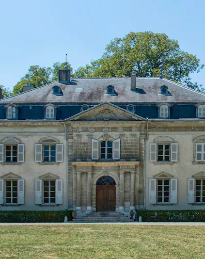 Voltaire Castle facade with arched entrance and shuttered windows, surrounded by greenery.