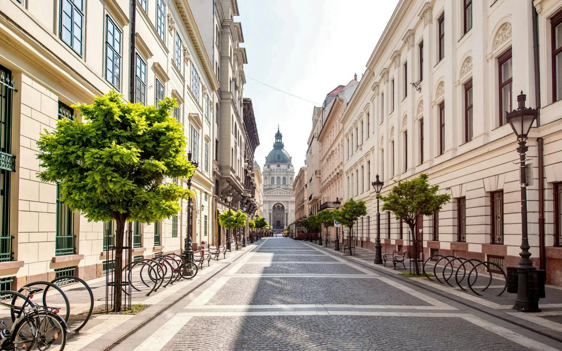 Zrínyi Street in Budapest leading to St. Stephen's Basilica, lined with trees and historic buildings.