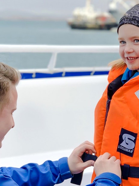 Tour guide assisting guest with life jacket on Reykjavik puffin watching boat tour.