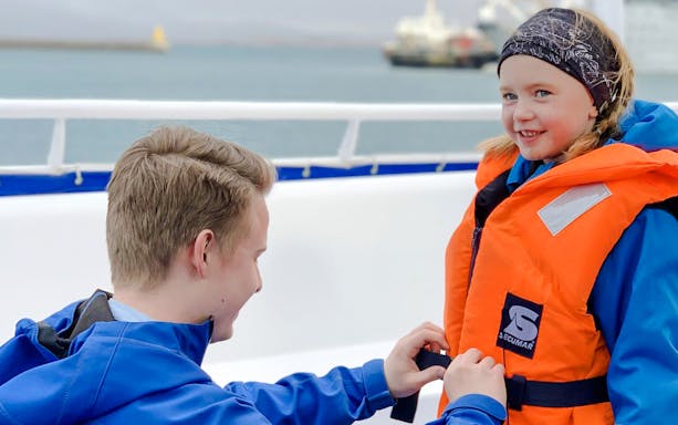 Tour guide assisting guest with life jacket on Reykjavik puffin watching boat tour.