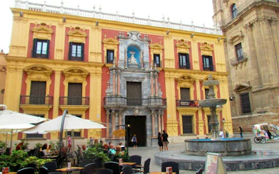 Facade of the Episcopal Palace in Malaga with a fountain in the foreground.