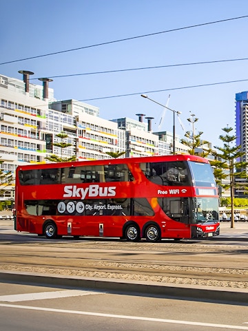 SkyBus traveling from Melbourne International Airport with city buildings in the background.