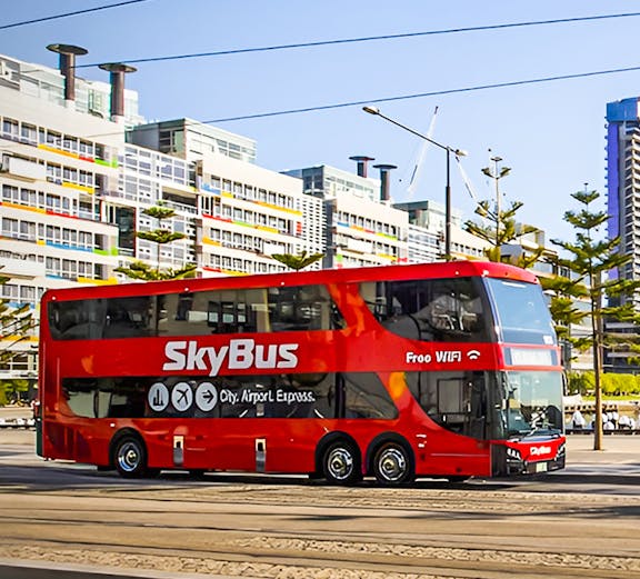SkyBus traveling from Melbourne International Airport with city buildings in the background.