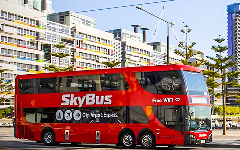 SkyBus traveling from Melbourne International Airport with city buildings in the background.