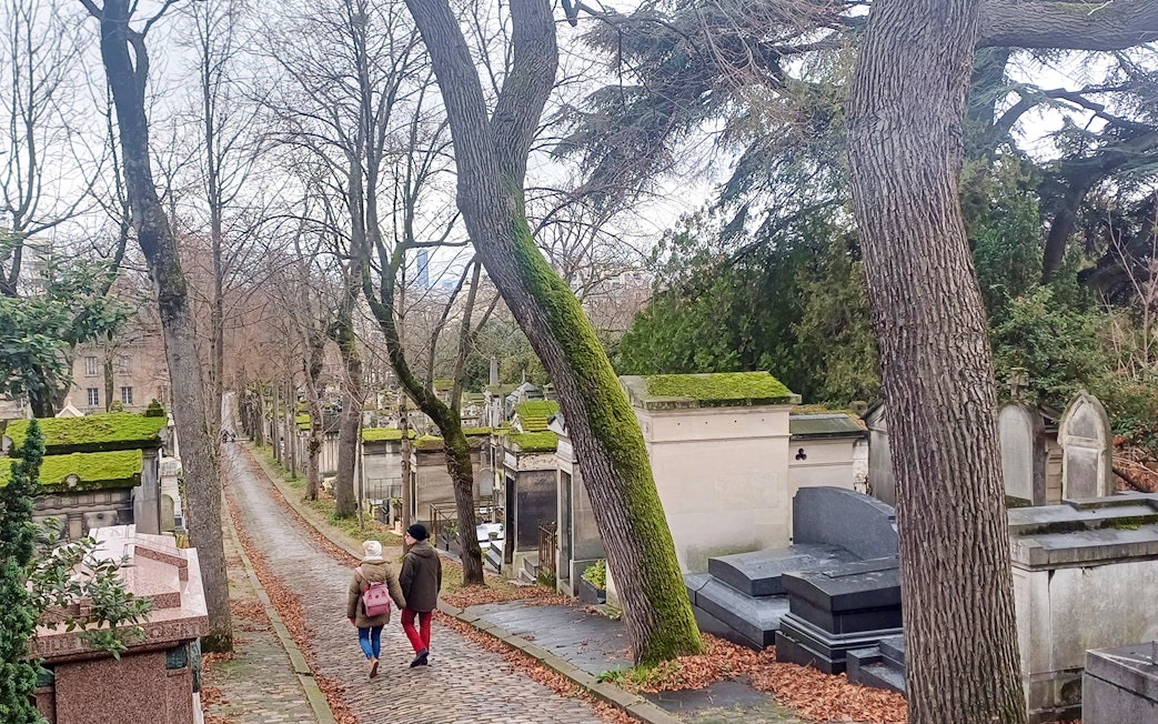 Visitors walking along a path in Père Lachaise Cemetery, Paris, France.