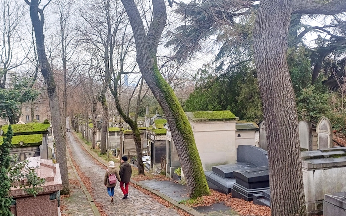 Visitors walking along a path in Père Lachaise Cemetery, Paris, France.