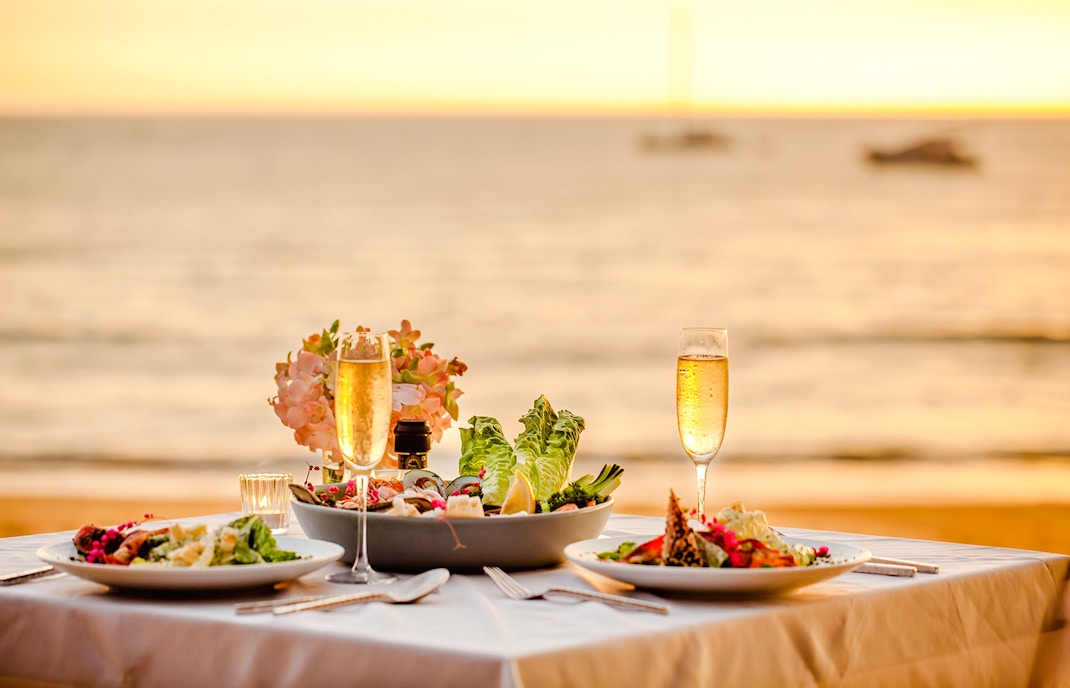 Romantic sunset dinner setup with champagne and salads by the ocean.