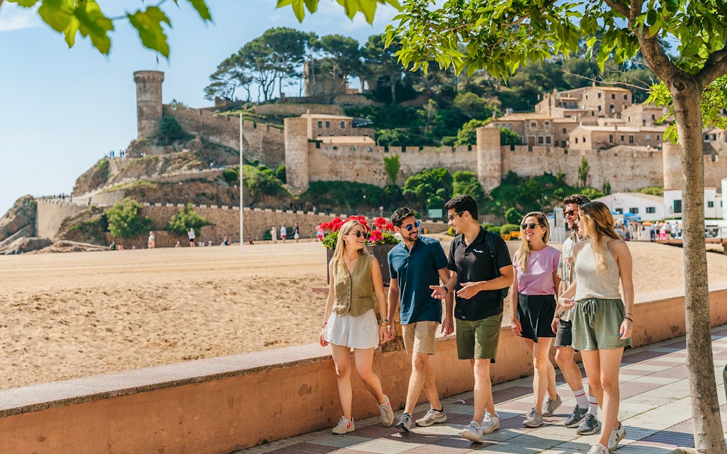 Tourists walking along the beach promenade near Tossa de Mar castle in Costa Brava.