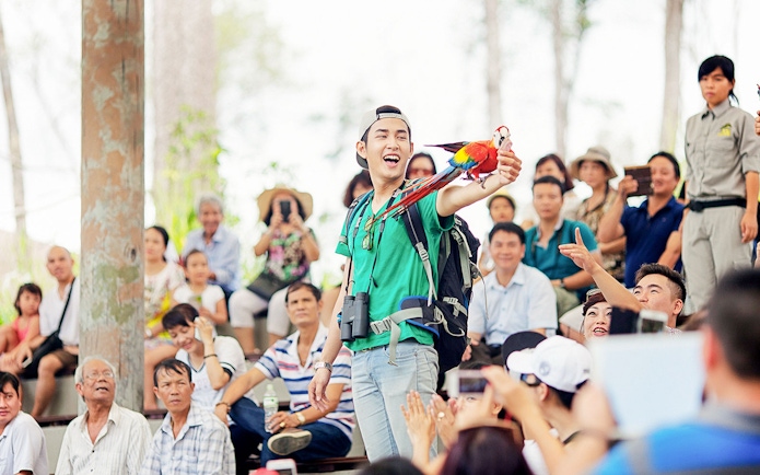 Man holding a colorful parrot during a bird show at Vinpearl, with an audience watching.