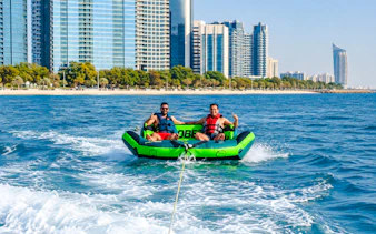 Two people enjoying a donut ride on the water with Abu Dhabi skyline in the background.