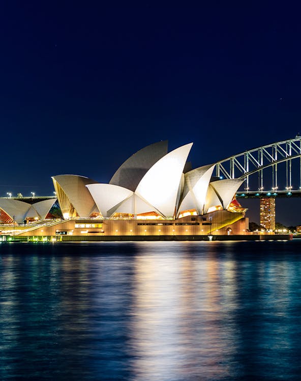 Sydney Opera House and Harbour Bridge illuminated at night, viewed from the water.