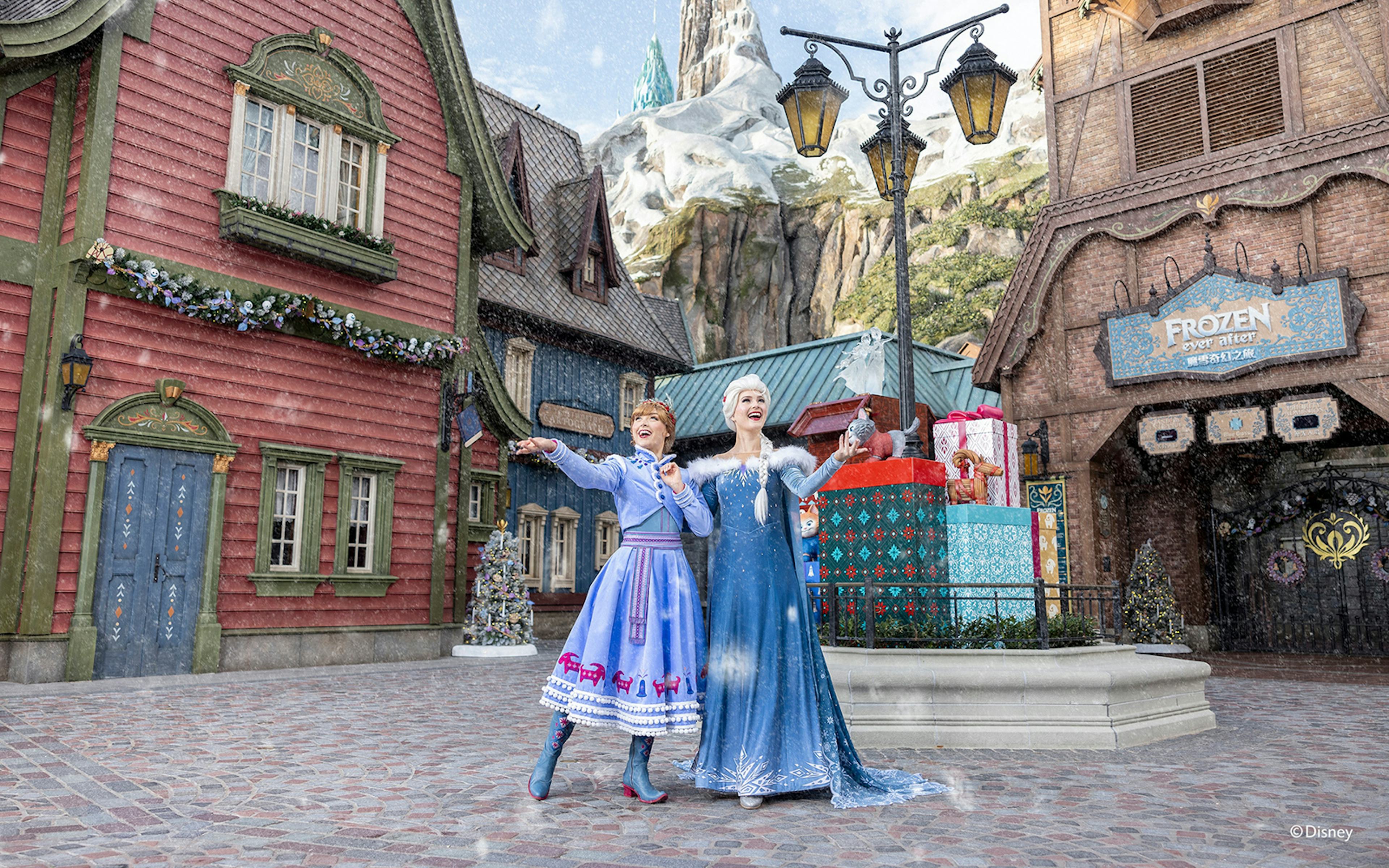 Characters in winter attire at Frozen-themed area, Disneyland Hong Kong, with snow and festive decorations.