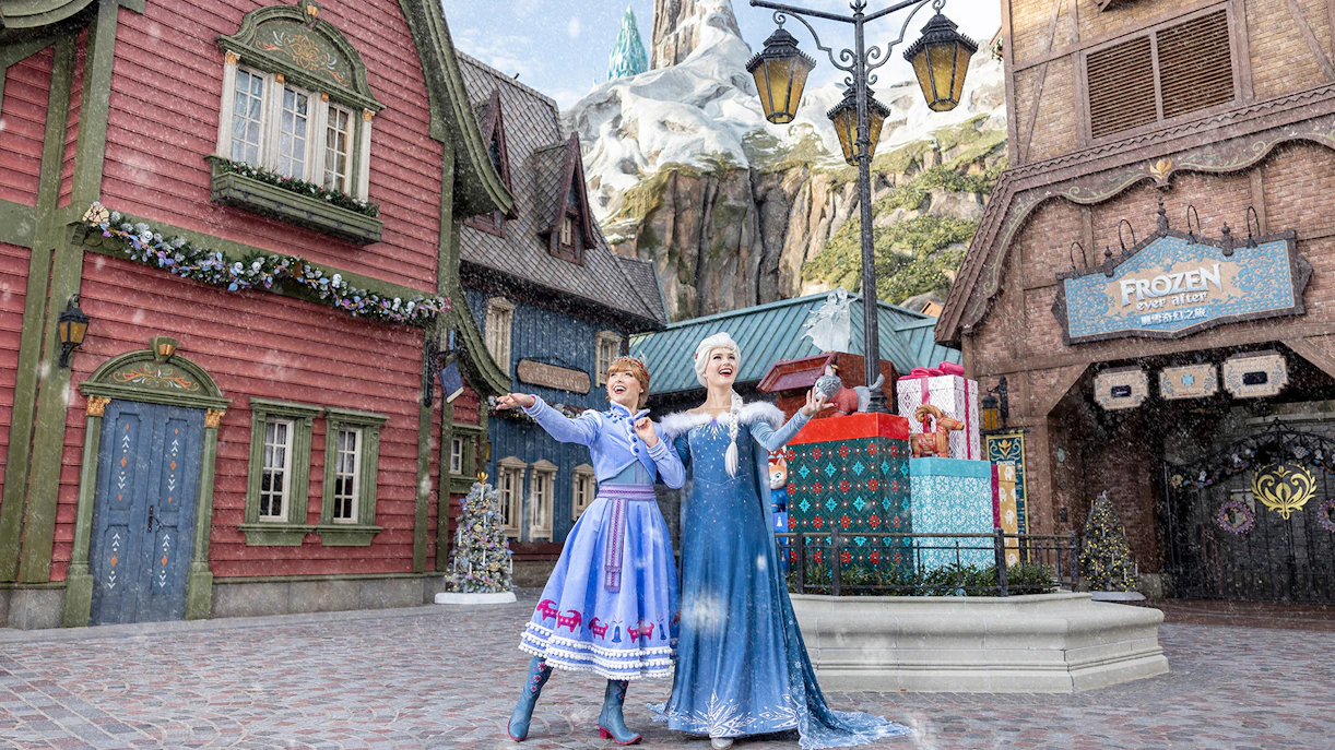 Characters in winter attire at Frozen-themed area, Disneyland Hong Kong, with snow and festive decorations.