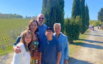 Family enjoying Tuscan vineyard tour with cypress trees and distant scooter group.