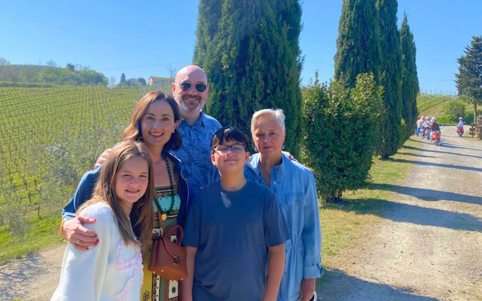 Family enjoying Tuscan vineyard tour with cypress trees and distant scooter group.