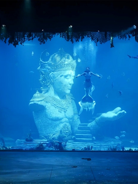 Underwater performance with mermaid near Varuna statue in theatrical dining experience.