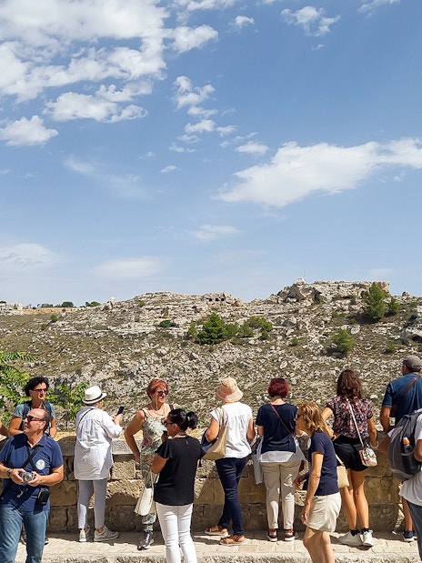 Tourists overlooking the rocky landscape of Matera during a bus tour with audio guide.